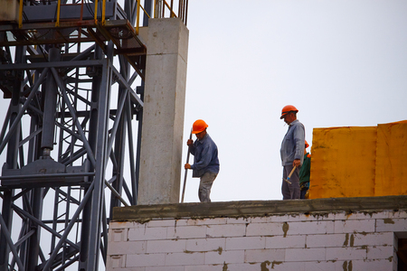 Kharkiv, Ukraine - August 02, 2019: Male builders work on the construction of a multi-story cement building, the formation of cement supports in prefabricated forms against a blue sky, selective focusのeditorial素材