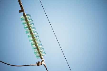 Close up bottom view of insulators on high-voltage wires on a power tower against a blue skyの写真素材