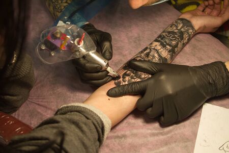 Kharkiv, Ukraine - April 08, 2017: Close-up of the hand of a tattoo master in black gloves with a tattoo machine makes a tattoo according to the sketchのeditorial素材