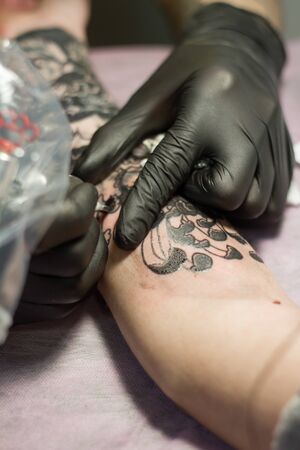 Kharkiv, Ukraine - April 08, 2017: Close-up of the hand of a tattoo master in black gloves with a...