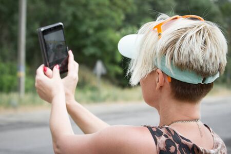 Adult blonde woman makes selfie on smartphone on a background of a field of sunflowers, selective...