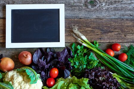 Fresh vegetables and herbs on an old rough wooden surface and chalk board for inscription or menu, healthy eating concept, selective focusの写真素材