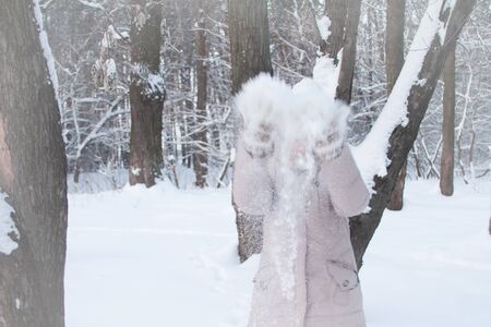 Young woman in winter clothes in snowy forest throws white snow and laughs, selective focus