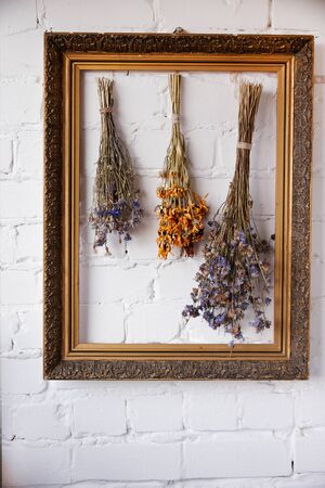 Three bunches of dried wildflowers in an old frame against white brick wall, selective focus