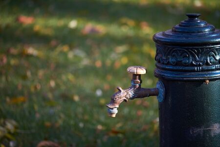 Close up of an old-style column with drinking water in an autumn park, selective focus