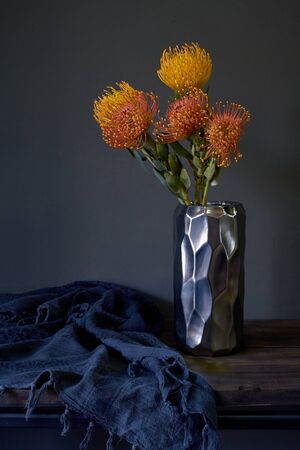 Bouquet of yellow and orange exotic protea flowers in metal vase on a dark background, selective...