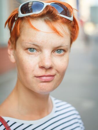 Close up portrait of a middle-aged red-haired woman looking at the camera and smiling on a blurred street background, selective focusの写真素材