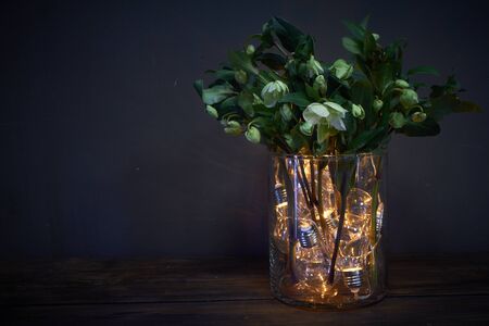 Glass vase filled with luminous bulbs and bouquet of hellebore, festive concept
