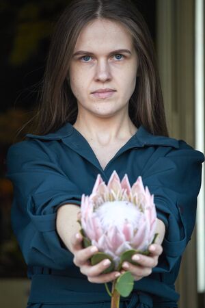 Portrait of girl with dark hair holds a pink huge protea, selective focus