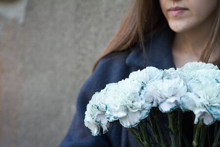 Girl with dark hair holds in her hands a bouquet of blue carnations on a gray wall background, selective focusの写真素材