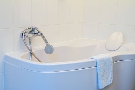 Modern corner bathtub with headrest, faucet and shower with long hose in the snow-white interior...