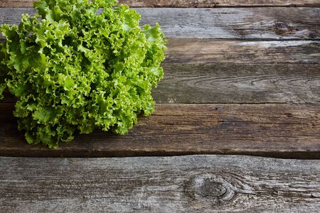 Head of green fresh salad with root on an old rough wooden surface, healthy eating concept,...