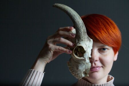 Portrait of a middle-aged redhead woman holding half goat skull in front of her face, duplicity conceptの写真素材