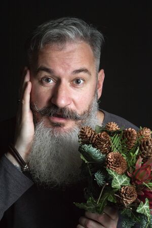 Middle-aged bearded man holding a winter bouquet of Nobilis fir twigs, cones, pistachio, leucodendron and ivy, winter gift conceptの写真素材