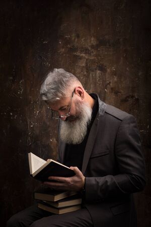 Portrait of a gray haired bearded man with glasses reading book in Russian, on the cover Russian inscription M. Gorky, selective focusの写真素材