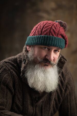 Studio portrait of handsome gray hair mature stylish man with beard and mustache dressed in warm...