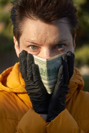 Middle aged european woman in protective black gloves holding dollar bills instead of a protective mask during coronavirus COVID-19 Epidemic, background or conceptの写真素材