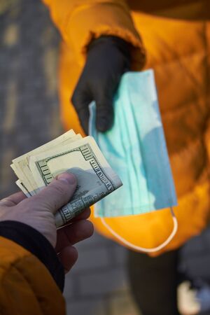 Hands exchange 100 dollar bills for surgical face mask signifying a spike in price of face mask during the corona virus pandemic of 2020の写真素材