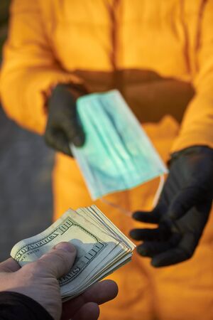 Hands exchange 100 dollar bills for surgical face mask signifying a spike in price of face mask...