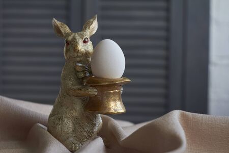 Spring composition, golden bunny figurine with egg on beige tablecloth, Easter concept, selective...