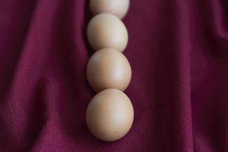 Natural eggs on red tablecloth, few brown chicken eggs lie on burgundy tablecloth, selective focus