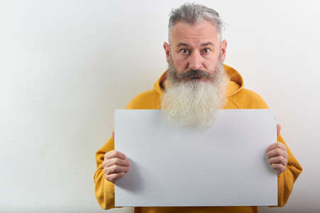 Portrait of mature gray-haired bearded man with blank sheet over white background, selective focusの写真素材