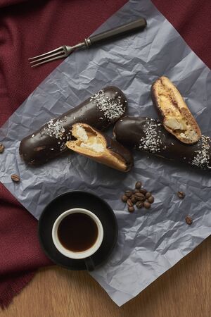 Pastry filled with vanilla cream, traditional french eclairs with chocolate and cup of espresso, selective focus.の写真素材