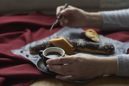 Woman eating eclairs filled with vanilla cream, traditional french eclairs with chocolate and cup of espresso, selective focus.の写真素材