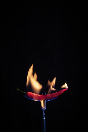 Vintage fork with burning chili pepper on black backdrop, selective focusの写真素材