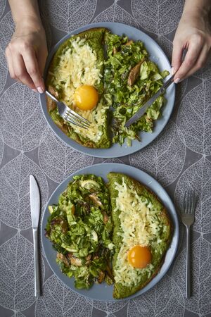 Top view of two plates with omelet and salad on table, female hands are holding cutlery. Family meal concept.の写真素材