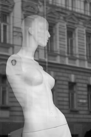 One white naked mannequin displayed in shop window with city lights and buildings reflections on the glass, selective focusの写真素材