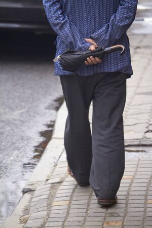 Back view of mature man walking on the street with umbrella, selective focusの写真素材