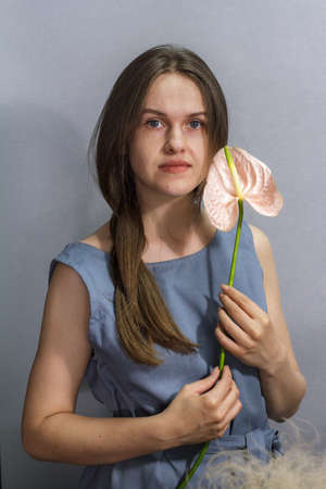 Sensual portrait of long-haired brunette girl with one pink Anthurium flower on gray backgroundの写真素材