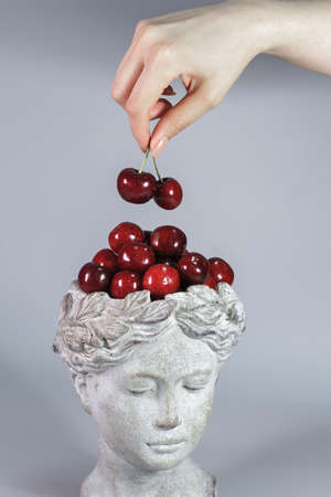 Stylish decoration made in shape of Greek goddess head full of red ripe cherries. Beautiful design...