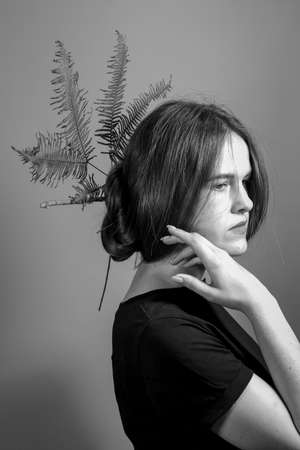 Black and white portrait of brunette girl with crown of fern in her hair, gray background. Stylish Hairstyle with Golden Umbrella Fern.の写真素材