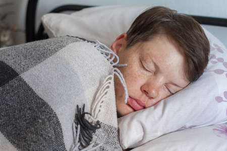 Mature brunette woman sleeping in bed under plaid blanket, concept of illness or cold, treatment at home, selective focusの写真素材