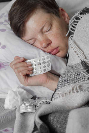 Mature brunette woman sleeping in bed under plaid blanket, concept of illness or cold, treatment at home, selective focusの写真素材