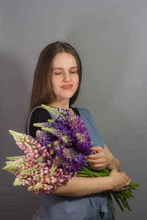 Brunette florist girl with bouquet of multi-colored lupins on gray background, woman florist with bouquet isolate, selective focusの写真素材