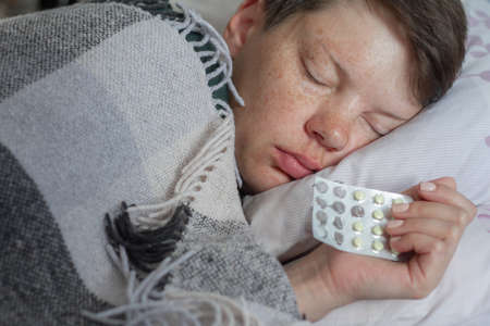 Mature brunette woman sleeping in her bed under plaid blanket, concept of illness or cold, treatment at home, selective focusの写真素材