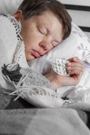 Mature brunette woman sleeping in her bed under plaid blanket, concept of illness or cold, treatment at home, selective focusの写真素材