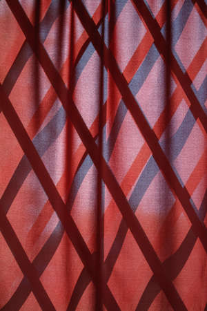 Red wavy natural fabric curtain over wooden partition made of bamboo slats, natural oriental decor, selective focusの写真素材
