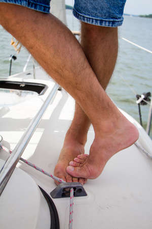 Male captain bare feet stands on deck of his yacht. Shine Yacht tackle during voyage, sailing concept.の写真素材