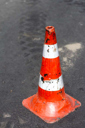 Worn down old traffic cone with white and orange stripes standing isolated on the streetの写真素材