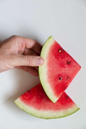 Male hahd holding slice of ripe red watermelon on white background, top viewの写真素材