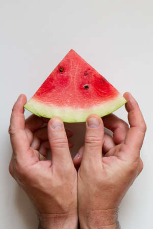 Male hahds holding slice of ripe red watermelon on white background, top viewの写真素材