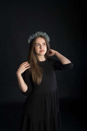 Studio portrait of beautiful brunette girl in wreath of dried flowers on black background, emotional conceptの写真素材