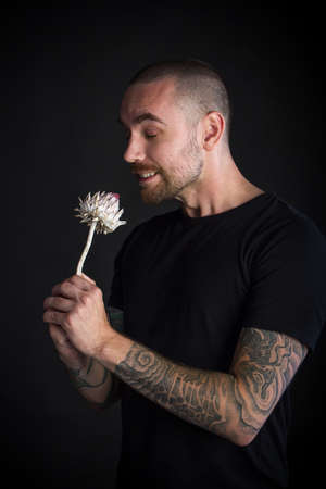 Portrait of young man holding single dry artichoke flower on black backgdrop, greeting card or conceptの写真素材