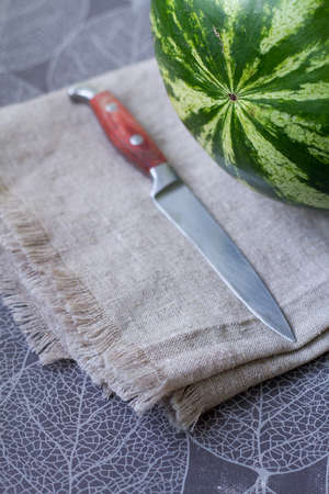 Fresh ripe watermelon on linen tablecloth next to knife, preparing for picnic, selective focus