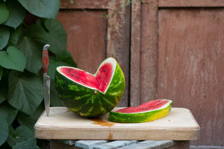 Fresh red ripe watermelon on wooden cutting board near old door to village house, picnic concept, selective focusの写真素材
