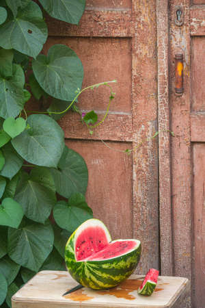 Fresh red ripe watermelon on wooden cutting board near old door to village house, picnic concept, selective focusの写真素材